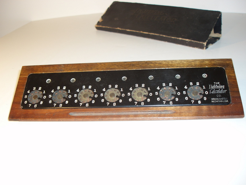 Figure 5 — A Grand Rapids Lightning Calculator on its sloped wooden base, the D-3 presentation, in black enamel, with its box lid behind.