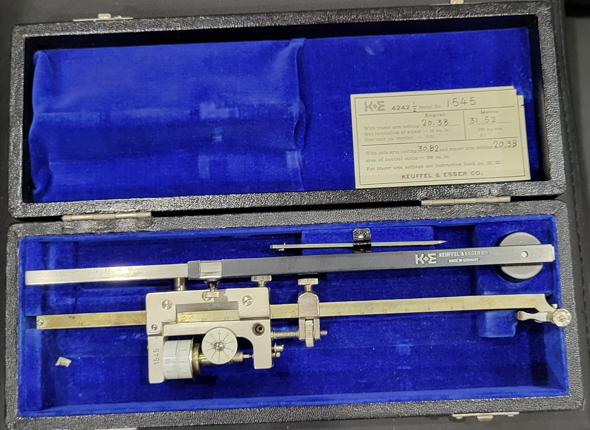 Figure 1 — My K&E 4242½, serial 1545, in its case: the steel tracer arm with its scale and the carriage, the brass pole arm, the round pole weight, and the settings card in the lid.