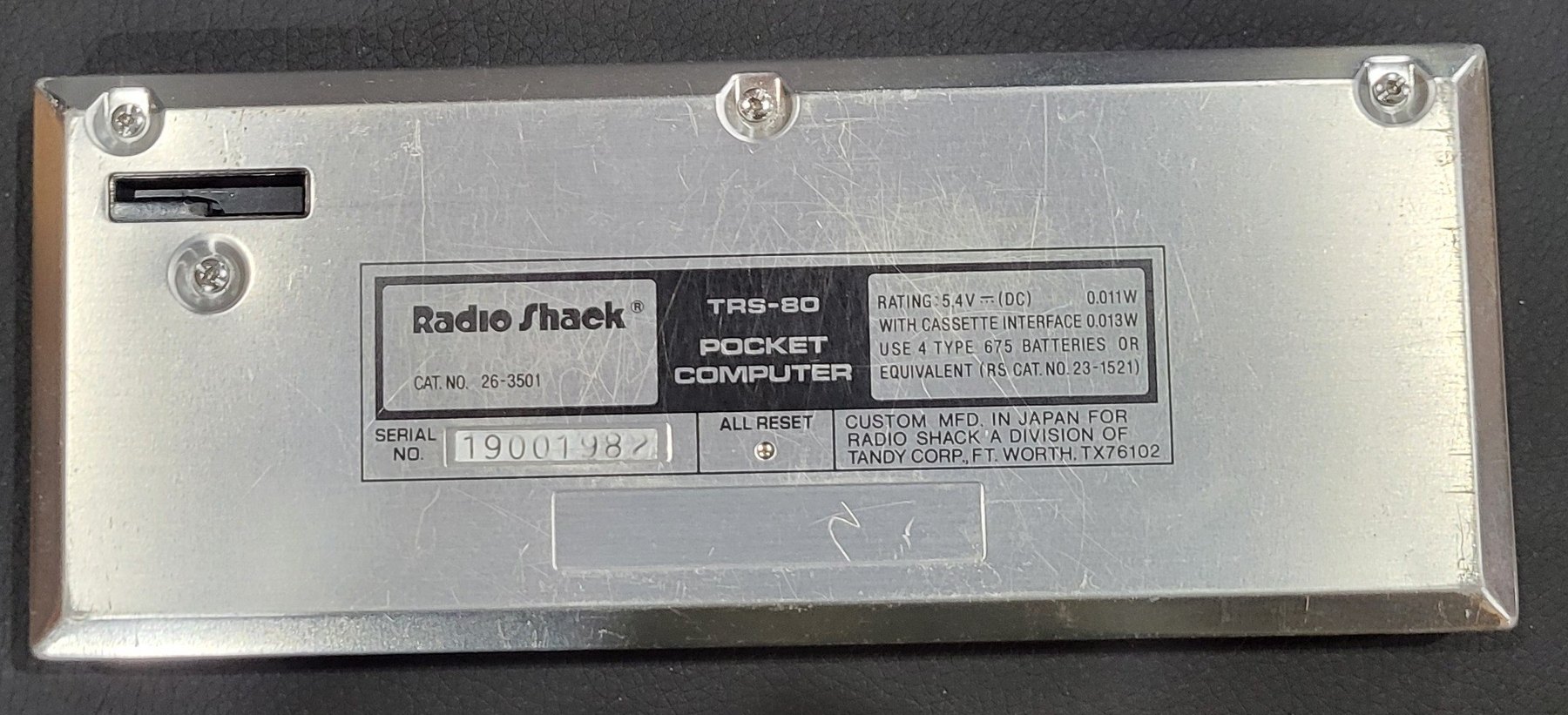 Figure 2 — The back of my PC-1: the Radio Shack label with the catalogue number, the power rating and the battery type, serial number 19001982, and the ALL RESET hole. The four case screws hold the back cover…