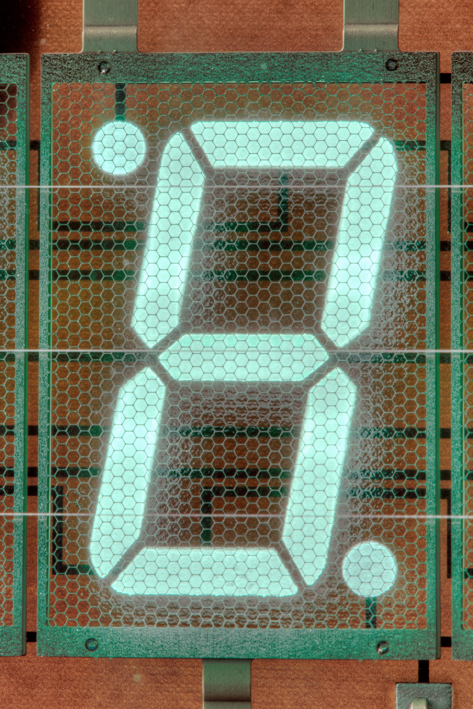 Figure 12 — A single digit of a modern vacuum-fluorescent display, close up: the mesh grid and the fine filament wires lie in front of the glowing segments, which are seen through them.
